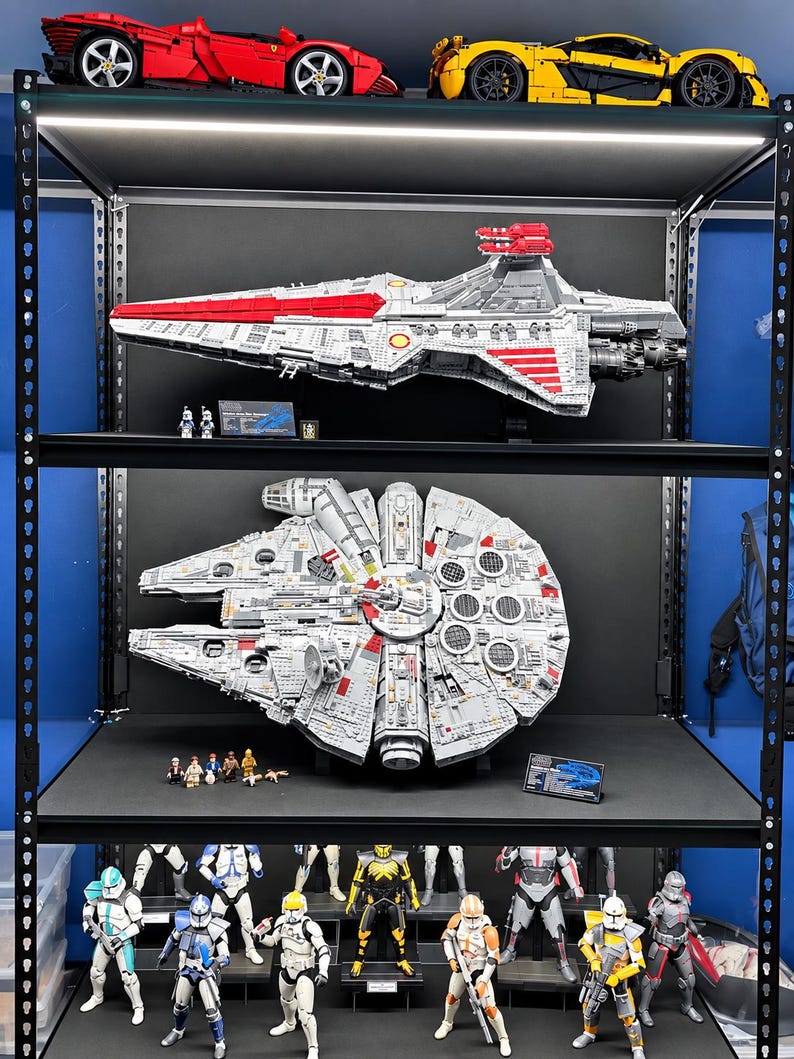 K&ouml;nnte beinhalten: Ein schwarzes Metallregal mit einem roten und einem gelben Sportwagen auf der obersten Ebene, einem gro&szlig;en grauen Raumschiffmodell mit zwei Minifiguren auf der zweiten, einem runden grauen Raumschiffmodell mit mehreren Minifiguren auf der dritten und verschiedenen Actionfiguren auf der untersten Ebene.