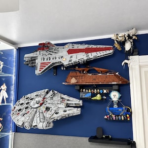 Pu&ograve; includere: Una collezione di modelli costruibili a tema Star Wars montati su una parete blu scuro, tra cui una grande astronave grigia e rossa, un mercantile circolare grigio, un sandcrawler marrone, un veicolo blu e varie piccole figure.