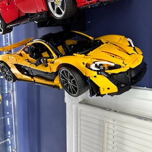 May include: A yellow and black model sports car with black wheels is displayed below a red model sports car. The yellow car has a sleek design with black accents. The red car is mounted above the yellow car.