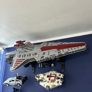 May include: A collection of Star Wars Lego spaceship models displayed on a blue wall. The largest model is a red and gray spaceship with a yellow stripe. The other models are a white and yellow spaceship, a black and gray spaceship, and a red and orange spaceship.