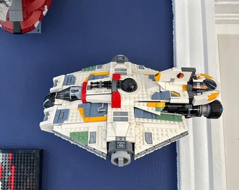 May include: A white, yellow, green, and red Lego spaceship with a black cockpit and a gray engine. The spaceship is mounted on a wall.