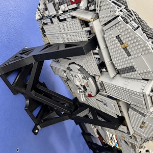 Pu&ograve; includere: Un grande e dettagliato modello di astronave realizzato con mattoncini di plastica grigi, montato su un supporto da parete nero angolare. Il modello presenta complesse texture meccaniche, torrette circolari e accenti rossi.