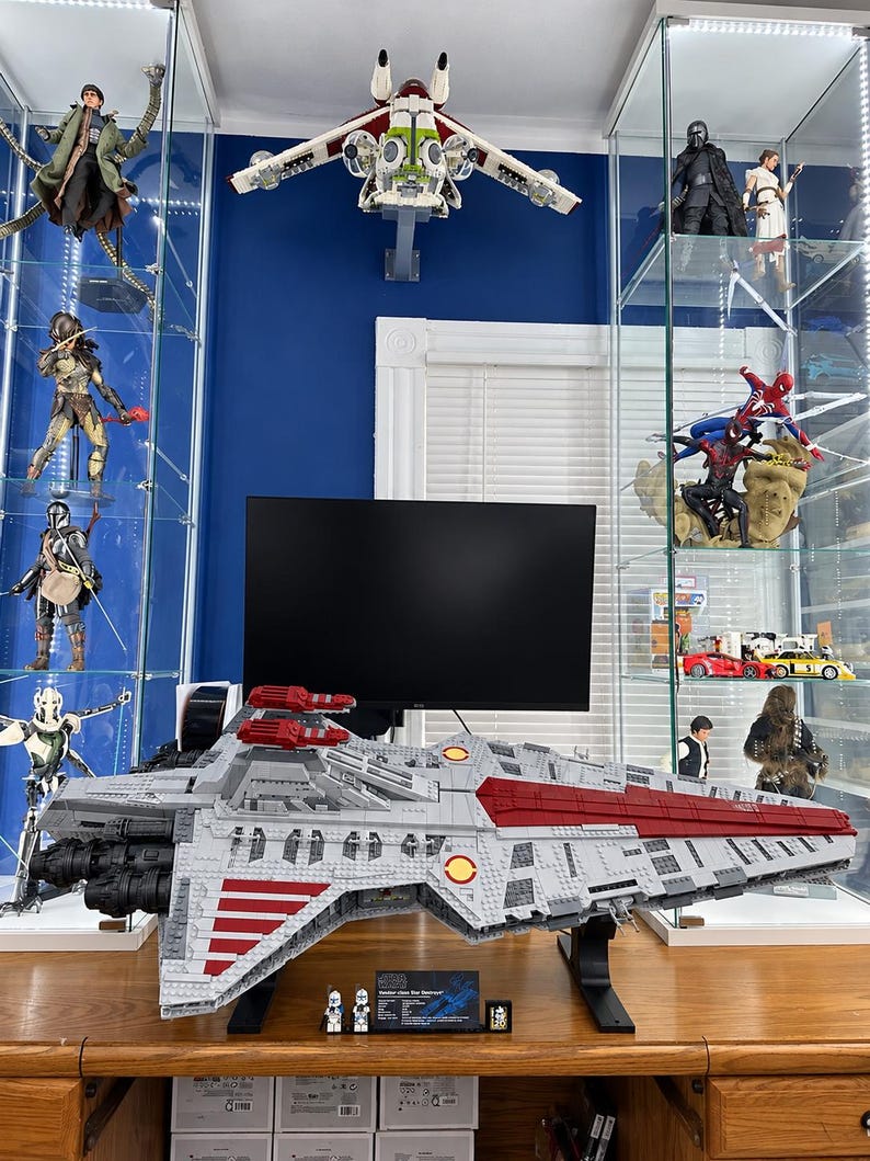 K&ouml;nnte beinhalten: Ein gro&szlig;es LEGO Star Wars Venator-class Star Destroyer Modell in Grau und Dunkelrot, auf einem schwarzen St&auml;nder mit zwei kleinen Minifiguren und einer Plakette. Das Schiff zeigt detaillierte Rumpfplatten, Triebwerke und rote Streifen.