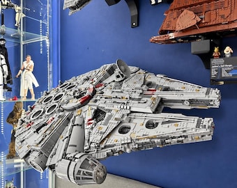 Può includere: Un grande e dettagliato modello dell'astronave Millennium Falcon realizzato con mattoncini in plastica grigia, caratterizzato da complesse texture meccaniche, un'antenna radar circolare e accenti rossi, montato su una parete blu.