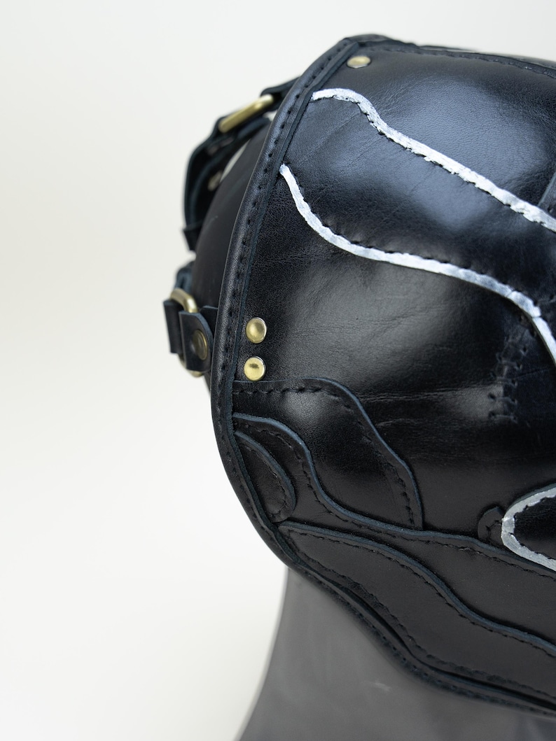 May include: Black leather satchel with silver accent stitching and brass hardware. The bag features decorative cutouts and a shoulder strap. The bag is shown against a white background.