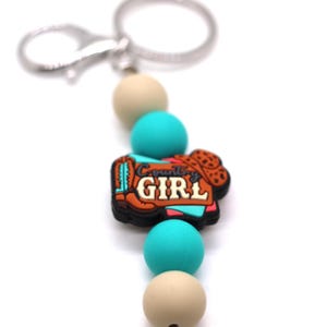 May include: A turquoise and beige silicone beaded keychain with a brown boot charm that says "Country Girl".