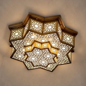 May include: A star-shaped flush mount ceiling light fitting with a metallic bronze finish. The fitting features intricate laser-cut geometric patterns that allow light to shine through, creating a detailed lattice effect across the entire surface.