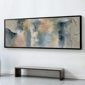 Op de afbeelding: Een groot rechthoekig wandkunstwerk met een abstracte compositie met dikke, getextureerde lagen. Het kleurenpalet bevat gedempte tinten blauw, saliegroen, zachtroze en crème, omlijst door een dunne zwarte rand.