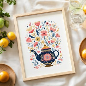 以下が含まれることがあります： フローラルデザインのネイビーブルーのティーポットが描かれた額入りのアートプリント。ティーポットはピンク、黄色、青の花でいっぱいです。プリントは明るい木製のフレームに入っており、背景は白です。画像は、レモンとトマトのある白い表面にあります。