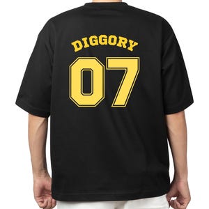 Könnte beinhalten: Schwarzes T-Shirt mit dem Wort "DIGGORY" und der Nummer "07" in gelben Blockbuchstaben auf dem Rücken. Das T-Shirt hat kurze Ärmel und einen Rundhalsausschnitt. Die Person, die das T-Shirt trägt, ist dem Betrachter abgewandt.