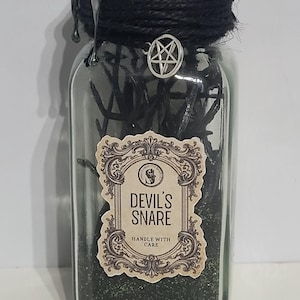 May include: A clear glass jar labelled "Devil's Snare" with a black twine-wrapped top and a silver pentagram charm. The jar contains dark green contents and a decorative label with the words "Handle With Care".