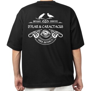May include: Black t-shirt with a white graphic design featuring two ravens perched on a branch with the text "Antiques & Oddities", "Dylar & Caractacus", and "Dark Artifacts".