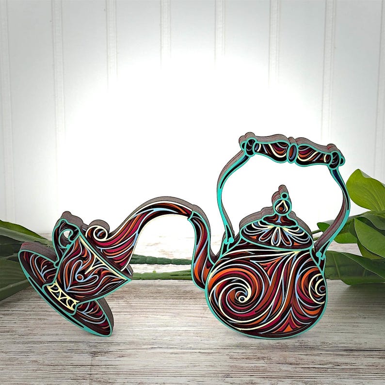 May include: A layered wooden wall art piece depicting a teapot pouring liquid into a teacup. The design features intricate swirling patterns in shades of deep red, orange, white, and black, with a vibrant turquoise outline defining the shapes.