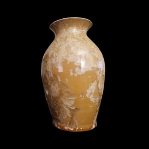 May include: A ceramic vase with a smooth, glossy finish featuring a warm tan base color. The surface is decorated with intricate, crystalline patterns in shades of cream and off-white that radiate across the body, creating a unique, organic texture.