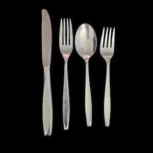 May include: A set of four silver-colored utensils: a knife, two forks, and a spoon. The knife is on the left, followed by a fork, a spoon, and another fork. All utensils have a sleek, modern design with a pointed handle.