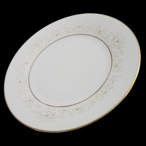 May include: A white porcelain dinner plate featuring a delicate embossed floral pattern along the rim. The plate is accented with a thin gold band around the inner circle and a gold-trimmed edge, creating a refined and classic appearance.