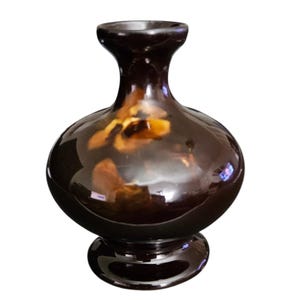 May include: A dark brown ceramic vase with a glossy finish. The vase has a bulbous body, a narrow neck, and a flared base. It features subtle, mottled patterns in shades of brown and tan, adding visual interest to the decorative piece.