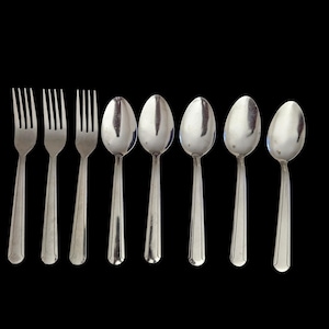 May include: A collection of silverware, including three forks and four spoons, arranged against a black background. The forks have four tines, and the spoons have oval bowls. The silverware is made of a shiny, reflective metal.