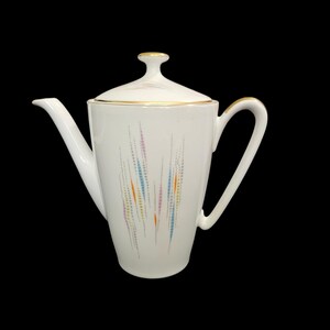 May include: White ceramic coffee pot with a lid and a handle. The pot features a colorful, abstract design of vertical lines in blue, orange, and pink. Gold trim accents the lid and rim.