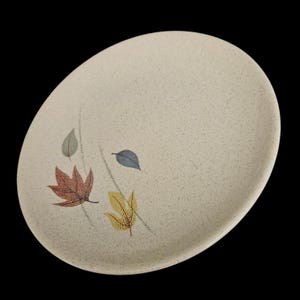 May include: Oval-shaped beige plate with a speckled surface. The plate features a design of colorful leaves in shades of red, yellow, blue, and gray. The leaves are arranged with delicate stems, creating a nature-inspired aesthetic.