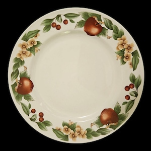 May include: Off-white ceramic plate with a decorative border featuring apples, cherries, green leaves, and small yellow flowers. The fruit and floral design is arranged around the rim of the plate, creating a classic, rustic aesthetic.