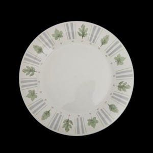 May include: A round white ceramic dinner plate featuring a decorative border pattern. The rim displays alternating light gray vertical stripes and green leaf illustrations, accented by small pink floral details between the motifs.