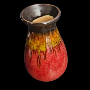 May include: A small, teardrop-shaped ceramic vase with a dark brown rim and a vibrant color gradient. The vase transitions from red at the base to yellow and orange, with dark brown streaks. The interior is a light beige color.