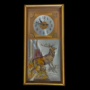May include: Rectangular wooden wall clock with a gold frame. The clock face is silver with black numbers and hands. Below the clock face is a picture of a deer in a forest setting. The clock is a vintage style.