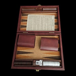 May include: Open backgammon set in a burgundy leather case. The game board features alternating brown and tan triangles. Includes dice, doubling cube, and playing pieces. The case is open, revealing the game's components.