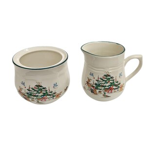 May include: A cream-colored ceramic sugar bowl and creamer pitcher set, each featuring a festive holiday illustration of a decorated Christmas tree, woodland animals, and birds, finished with a thin dark green rim along the top edges.
