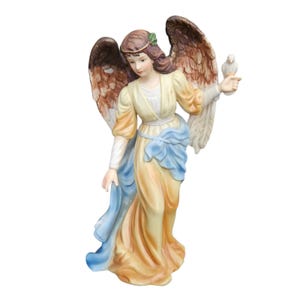 May include: A ceramic angel figurine featuring brown wings, a pale yellow dress with a blue sash, and brown hair adorned with a green leaf. The angel holds a small white bird on its left hand, with a serene expression and flowing garment details.