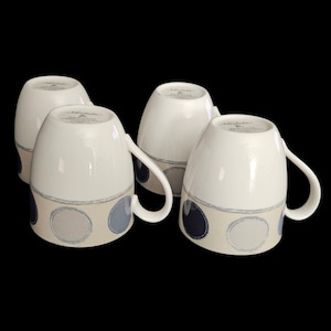 May include: Four white ceramic mugs with a cream-colored band featuring blue, gray, and navy blue circles. Each mug has a curved handle and a simple, elegant design. The mugs are arranged against a black background.