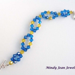 May include: A blue and yellow crystal bracelet with a silver toggle clasp. The bracelet is made with faceted crystals and is a delicate piece of jewelry.