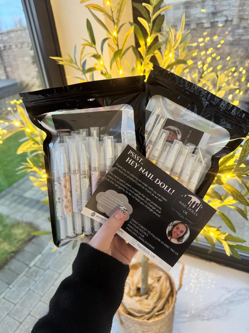May include: A black and white card with the text "PSSST.. HEY NAIL DOLL!" and "NAIL DOLLS UK" with a woman's face in the bottom right corner. The card is in front of a clear plastic bag filled with white nail polish bottles.
