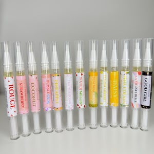 Pode incluir: Uma coleção de canetas de óleo para cutículas com vários aromas frutados e florais. Cada caneta tem um corpo de plástico transparente e um rótulo com um nome diferente, como "Morango" ou "Good Girl".