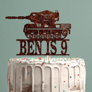 May include: Brown glitter tank cake topper with the text "BEN IS 9" on a white cake.