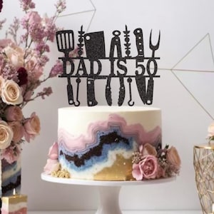 May include: A birthday cake with a black glitter cake topper that reads "DAD IS 50" with kitchen utensils. The cake has a white base with blue, pink, and gold wave-like designs. The cake sits on a white cake stand.