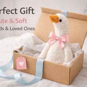 Puede incluir: Un peluche de ganso blanco con pico naranja y lazo rosa, presentado en una caja de cartón con una cinta azul claro y una etiqueta rosa con un corazón. El texto en la imagen dice "Perfect Gift, Cute & Soft, For Kids & Loved Ones."