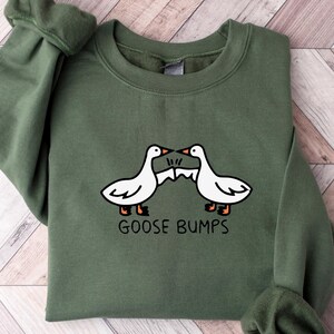 May include: A green sweatshirt with a white graphic of two geese facing each other with the text "Goose Bumps" underneath.