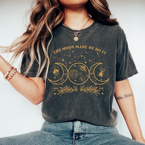 May include: A dark grey t-shirt with a graphic of three moons, stars, and the text "The Moon Made Me Do It".