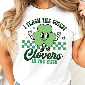 Könnte beinhalten: Weißes T-Shirt mit einem grünen Kleeblatt-Cartoon-Charakter, der Schuhe trägt und Friedenszeichen macht. Der Text auf dem Shirt lautet "Ich unterrichte die süßesten Kleeblätter im Beet".