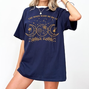 May include: A navy blue oversized t-shirt with a gold graphic of three moons, stars, and the text "THE MOON MADE ME DO IT".