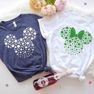 May include: Two t-shirts with a shamrock Mickey Mouse design. One shirt is navy blue with white shamrocks and the other is white with green shamrocks.