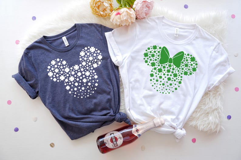 May include: Two t-shirts with a shamrock Mickey Mouse design. One shirt is navy blue with white shamrocks and the other is white with green shamrocks.