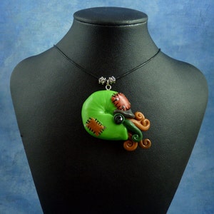 Puede incluir: Un collar con un colgante de pulpo cosido de color verde, marr&oacute;n y negro, en un cord&oacute;n negro.