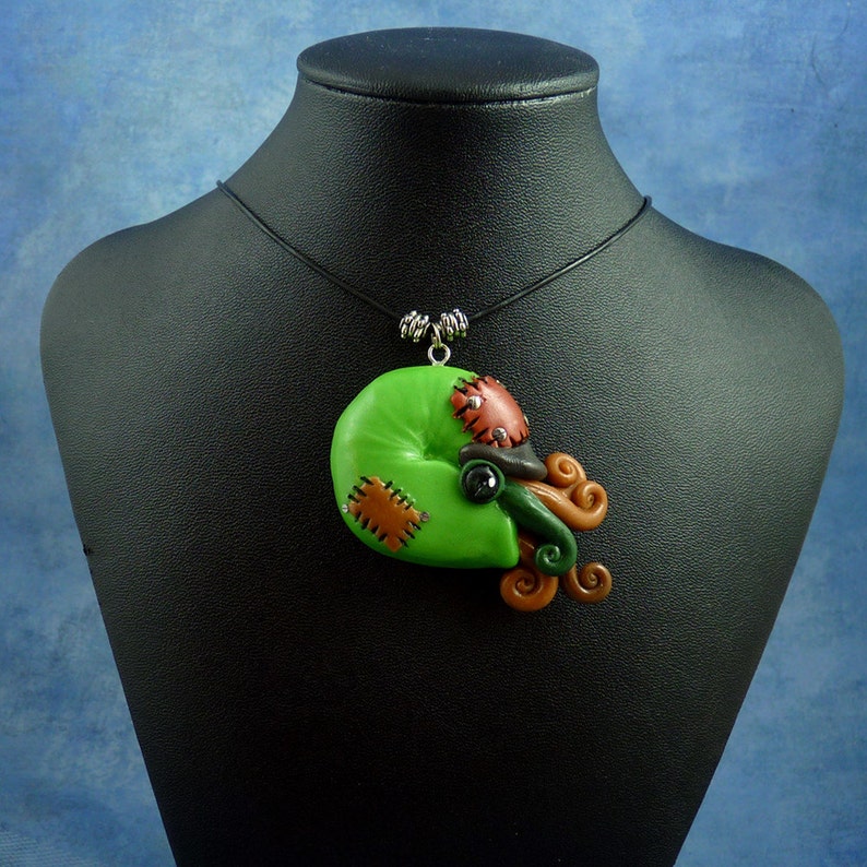 Puede incluir: Un collar con un colgante de pulpo cosido de color verde, marr&oacute;n y negro, en un cord&oacute;n negro.