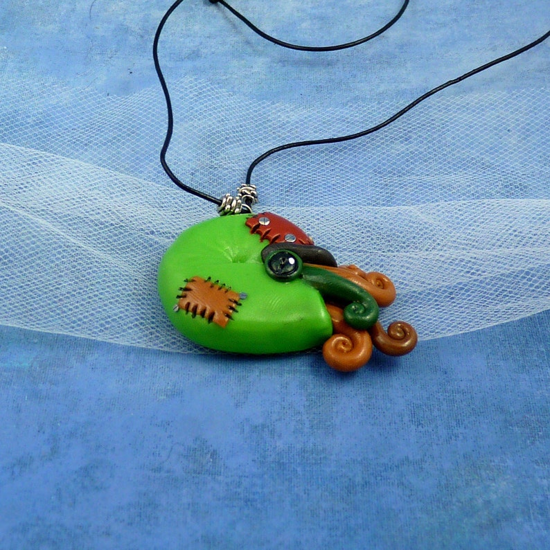 Puede incluir: Un collar verde, marr&oacute;n y negro con un colgante de coraz&oacute;n cosido y un dise&ntilde;o de tent&aacute;culo rizado.