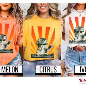 May include: Three t-shirts in melon, citrus, and ivory colors. Each shirt features a graphic of a cat wearing sunglasses and headphones, DJing with a retro sunburst design. The text on the shirts reads "Melon", "Citrus", and "Ivory".