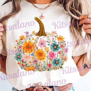May include: Cream-colored t-shirt featuring a white pumpkin design adorned with colorful flowers. The pumpkin has a golden stem and is surrounded by orange, pink, blue, and purple blooms. The word "Kitsalano" is printed on the shirt.