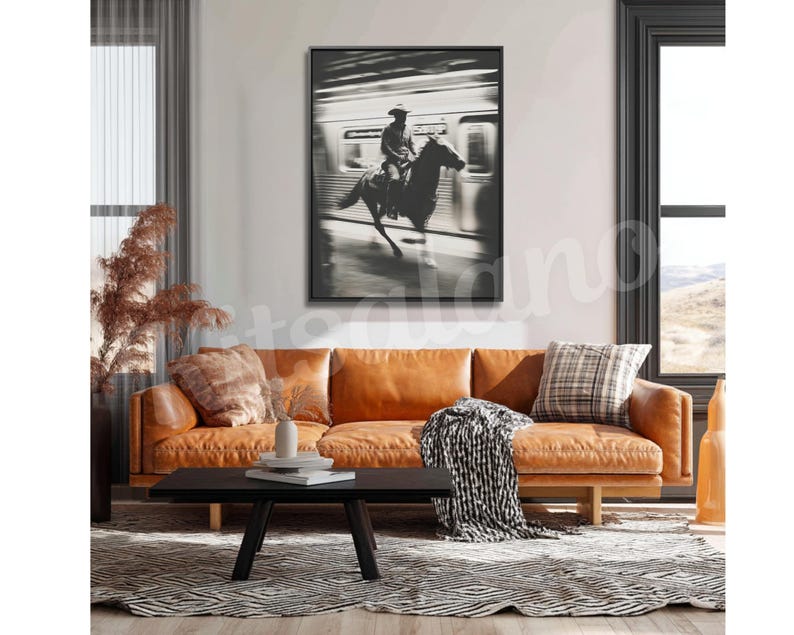 May include: Black and white framed print of a cowboy riding a horse inside a subway car. The artwork is displayed above a brown leather sofa with a black coffee table and a patterned rug.